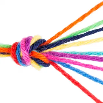 Mehrere bunte Wollfäden sind zu einem festen Knoten zusammengebunden, während die Enden lose auseinanderlaufen. Die Farben reichen von Rot, Blau und Grün bis zu Gelb und Pink.